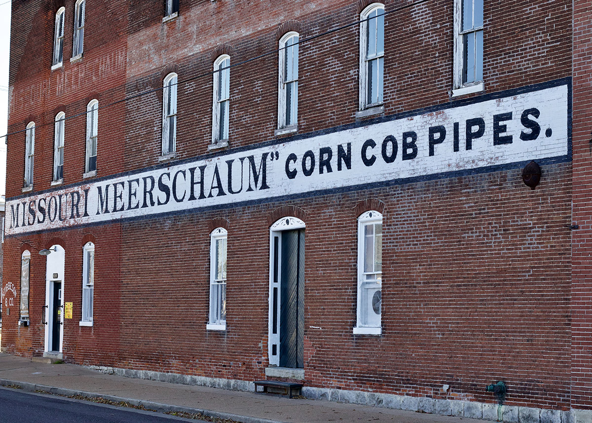 historical red brick building with chipped white letters that say missouri meershaum corn cob pipes