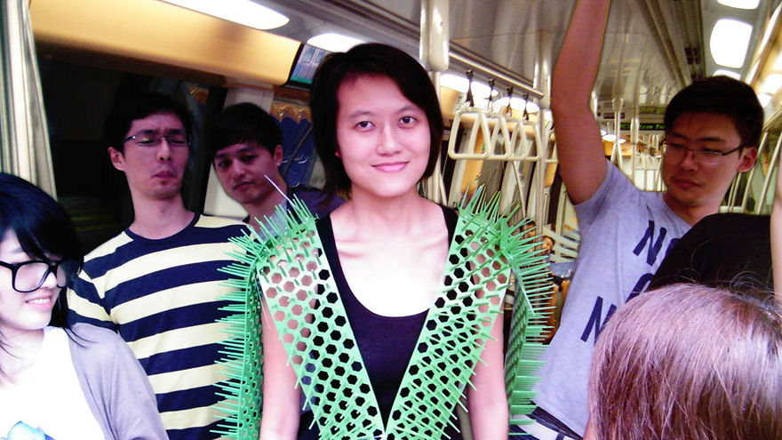 Images: A woman wears a green mesh "vest" of perforated material, complete with spikes out the sides to ward off fellow commuters on a train. Sharp ends extend from shoulders and arms to indicate personal space. Renderings exhibit the scale and operation of the material.