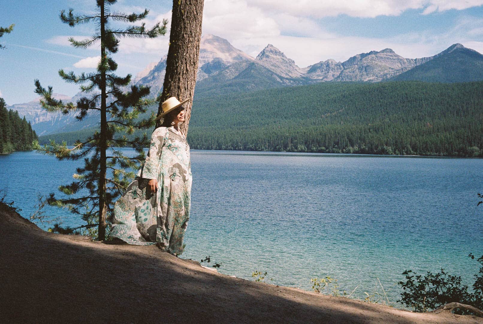 A woman in a kaftan looking across a lake with mountians in the background