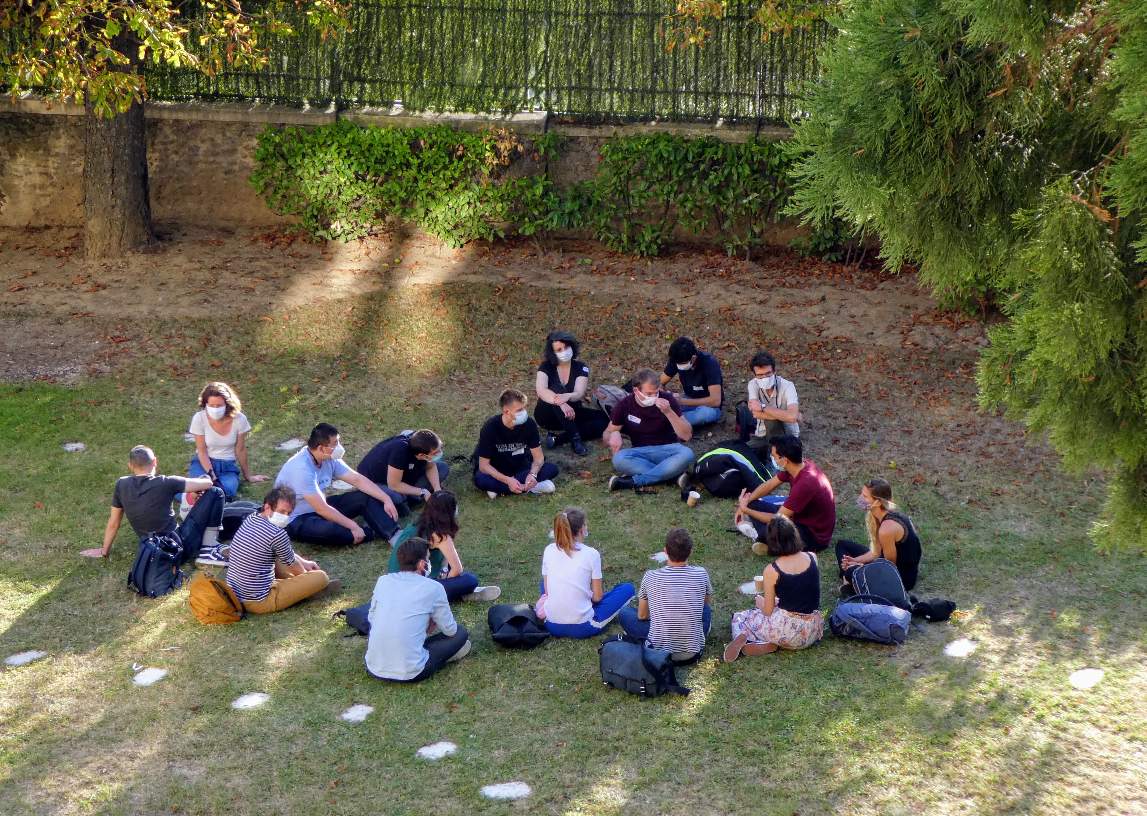 Une vingtaine de personnes sont assises dans l'herbe, en cercle. Elles échangent