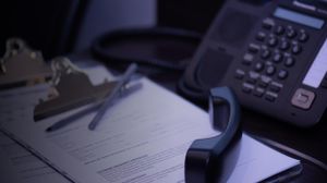 A close-up of a phone handset off the hook atop some clipboards with documents related patient intake at Glenbrook Dental