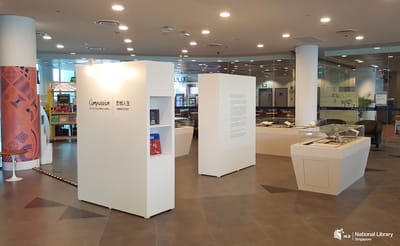A photo of the roving exhibition. An information wall in the middle is surrounded by showcases and a wall with books.