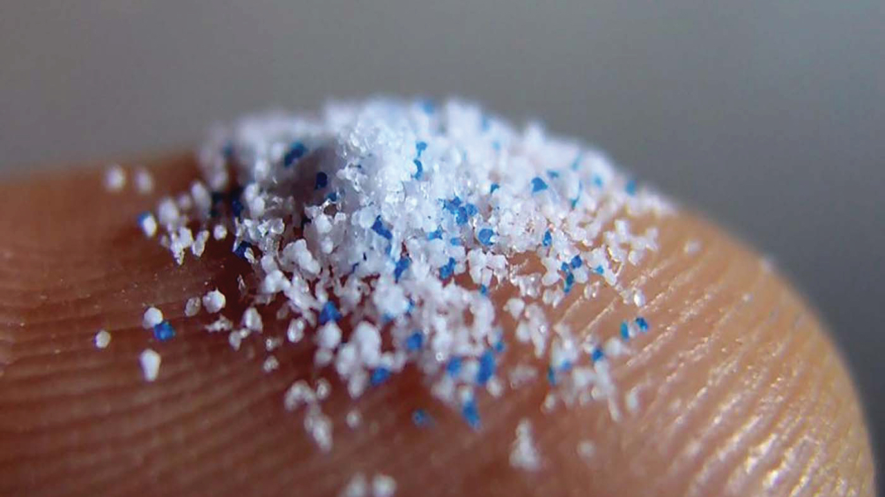Macro shot of a fingertip covered in tiny pieces of white and blue plastic