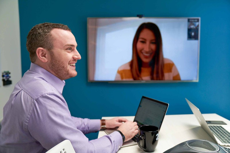 Smiling man typing on a laptop during a video conference