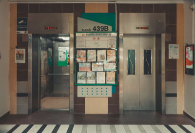 A ground floor lift lobby in Sengkang. A notice board separates an open lift on the left from a closed lift on the right.