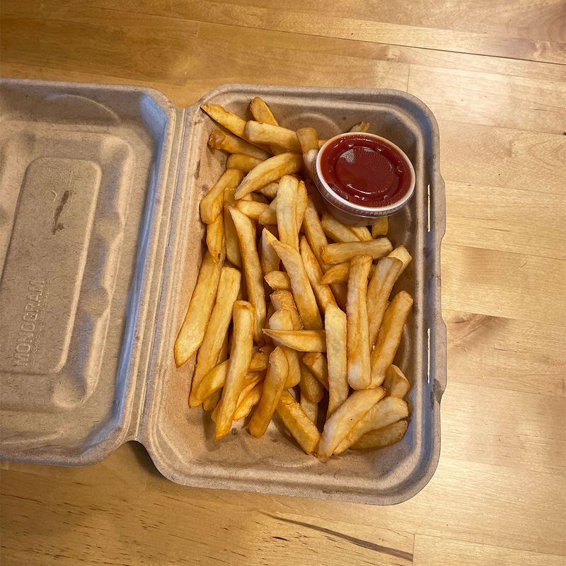 A basket of french fries with a small plastic container of ketchup in the top right corner.