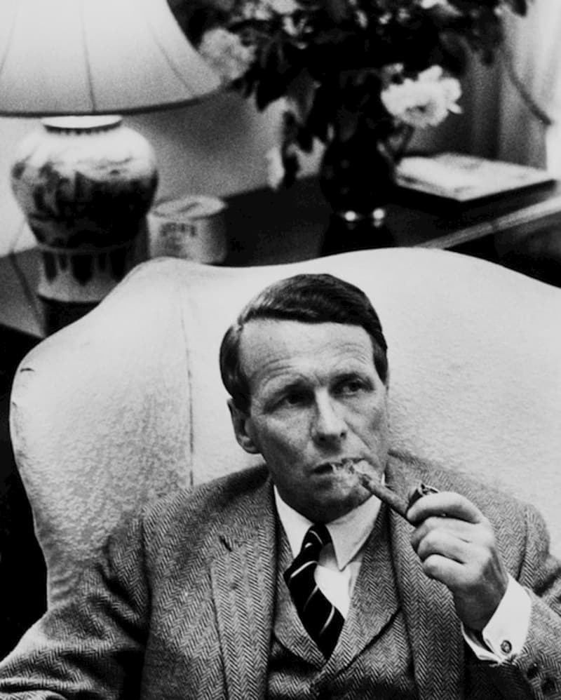 David Ogilvy sitting in an armchair, smoking a pipe.