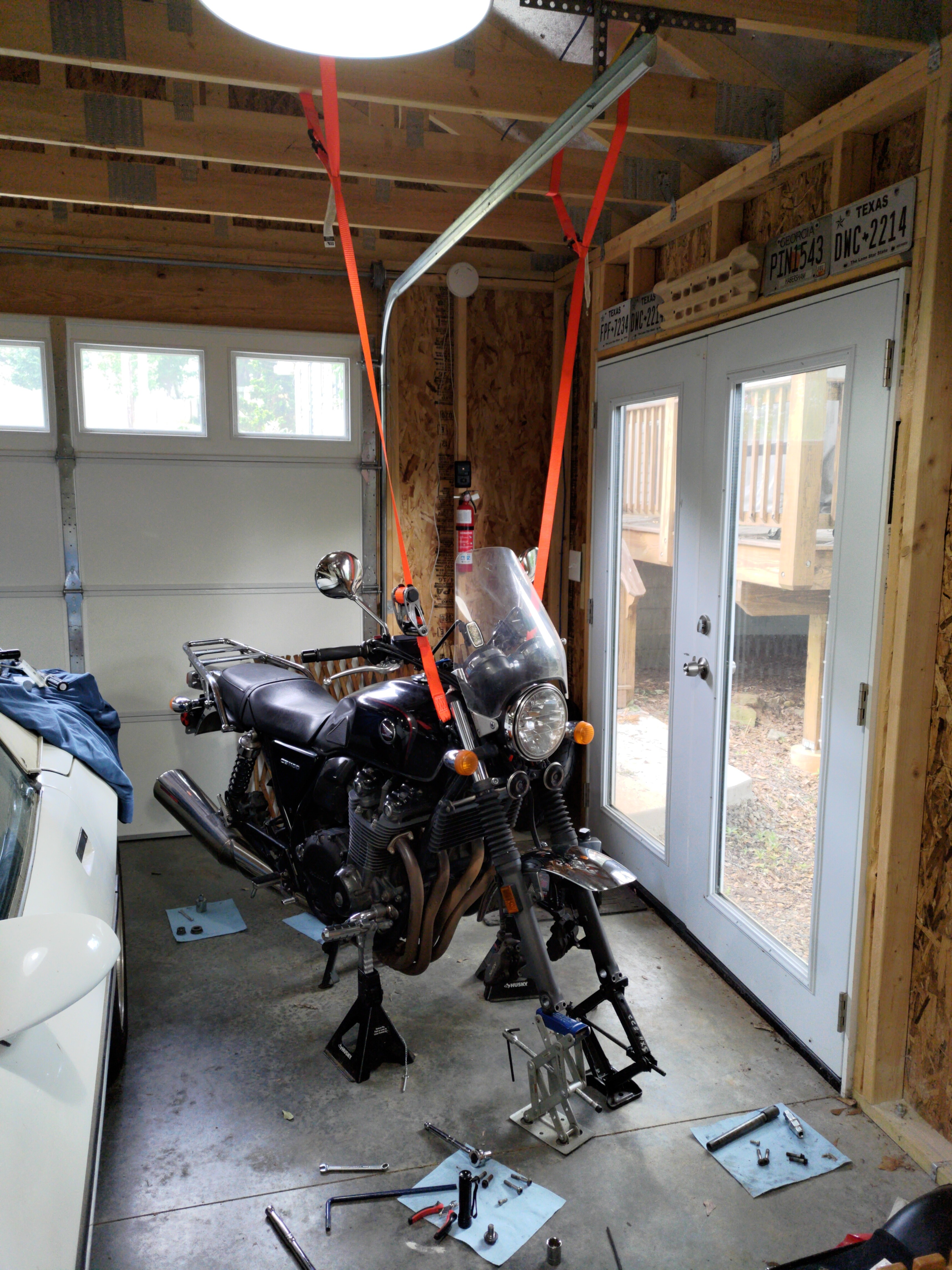 A motorcycle supported by its center stand and some ratchet straps looped over the ceiling joists and under the fork
