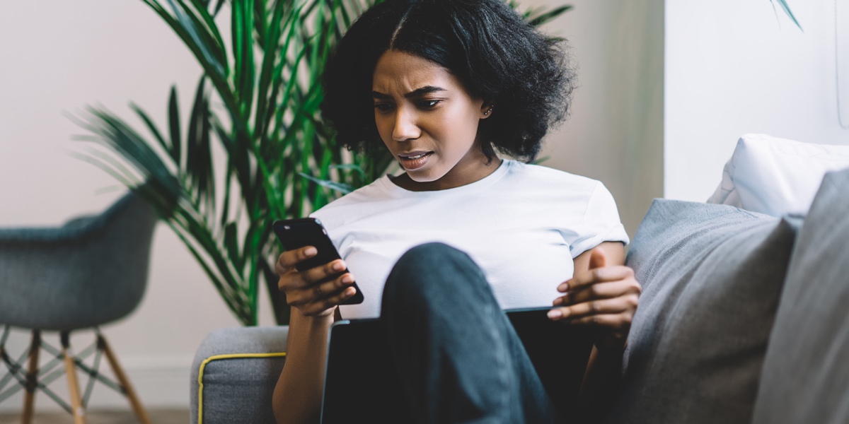 Woman at home, on the couch, trying to complete a task on a mobile app, appearing frustrated. Woman at home, on the couch, trying to complete a task on a mobile app, appearing frustrated.