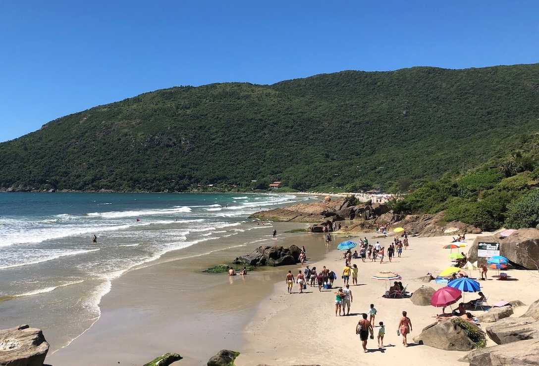 Vista da areia da praia com banhistas caminhando e mar a esquerda com poucas ondas