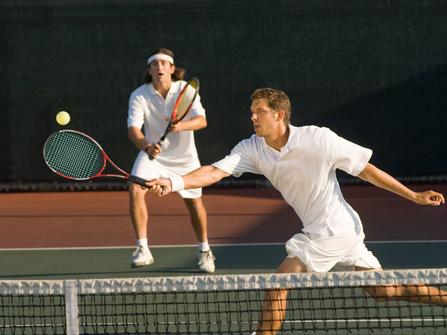 Two tennis players playing a doubles match with one hitting the ball at the net