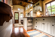 Timbercraft Tiny Homes' Denali gooseneck tiny house; interior of this home with light gray kitchen cabinets, loads of windows to bring in natural light and wood floors with rugs. Timbercraft Tiny Homes' Denali gooseneck tiny house; interior of this home with light gray kitchen cabinets, loads of windows to bring in natural light and wood floors with rugs.