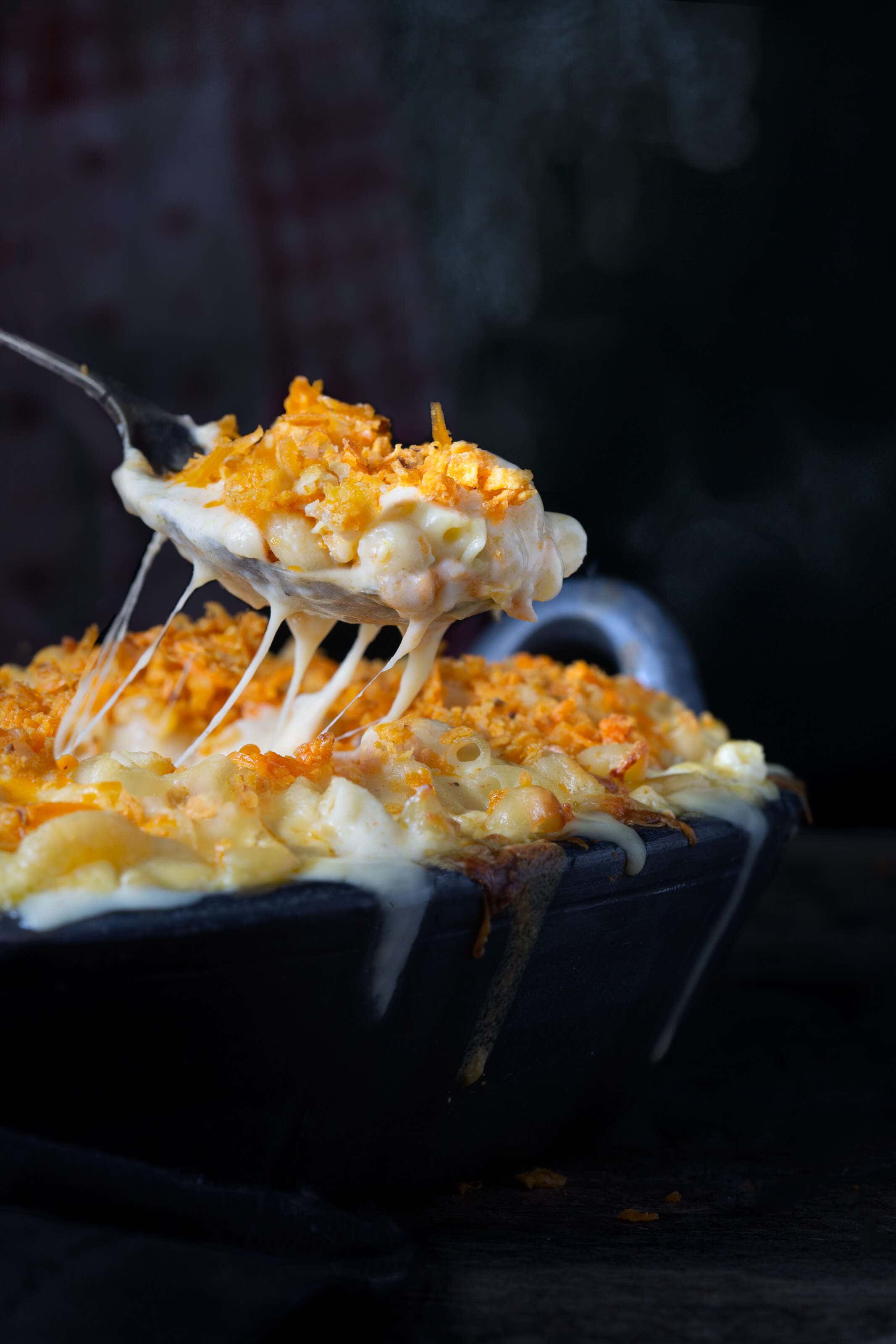Hot macaroni cheese being served with a spoon with steam rising from it.