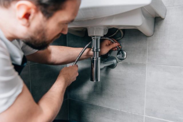 plumber in working overall fixing sink in bathroom