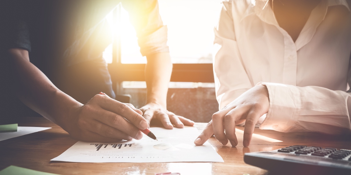 What is UX Strategy? Close up of two UX designers' hands as they stand at a desk and look over business goals