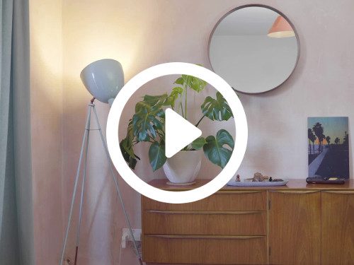 Home bedroom interior featuring circular wall mounted mirror above wooden drawer chest next to white adjustable lamp Zoom background