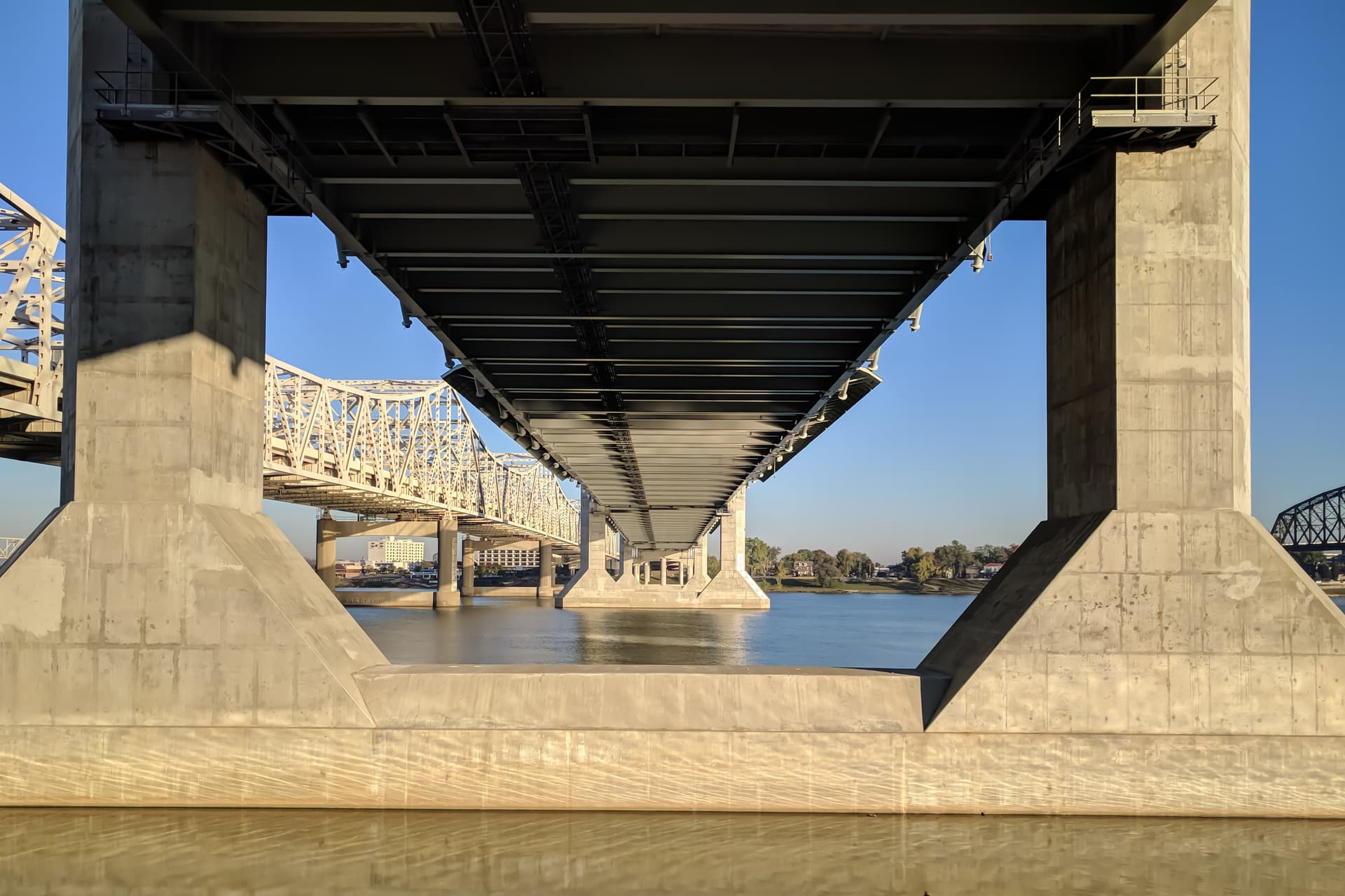 Looking towards Indiana across the Ohio River from underneath a bridge. The shot is framed by the bridge's concrete pylons, which regularly recede into the distance.