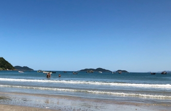 Foto da areia da praia com mar ao fundo e morro verde ao fundo