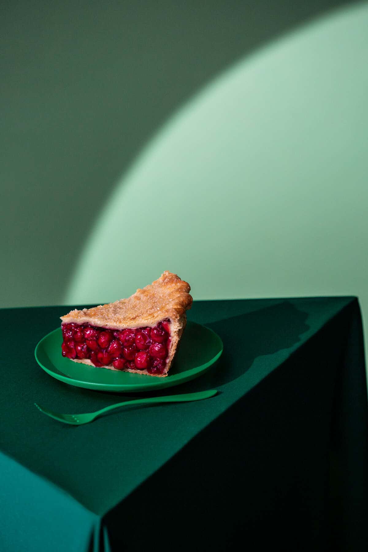 Cherry Pie sat on a green plate on a green table with a hard spotlight used to light the set