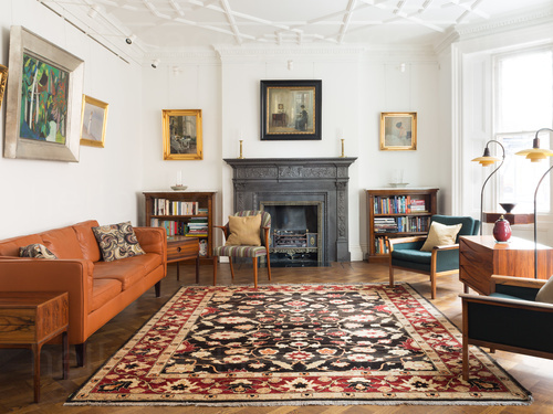 Classically styled living room featuring orange sofa with dark green chairs and large black fireplace Zoom background