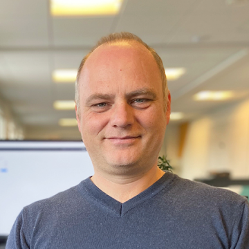 Profile picture of co-founder and advisor, Anders Wind smiling with sunshine and computer screen behind him.