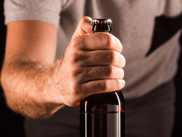 A man trying to open a bottle of beer with his thumb because he doesn't have a bottle opener