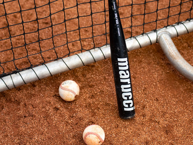 A Marucci fungo bat laying on a batting screen near two baseballs