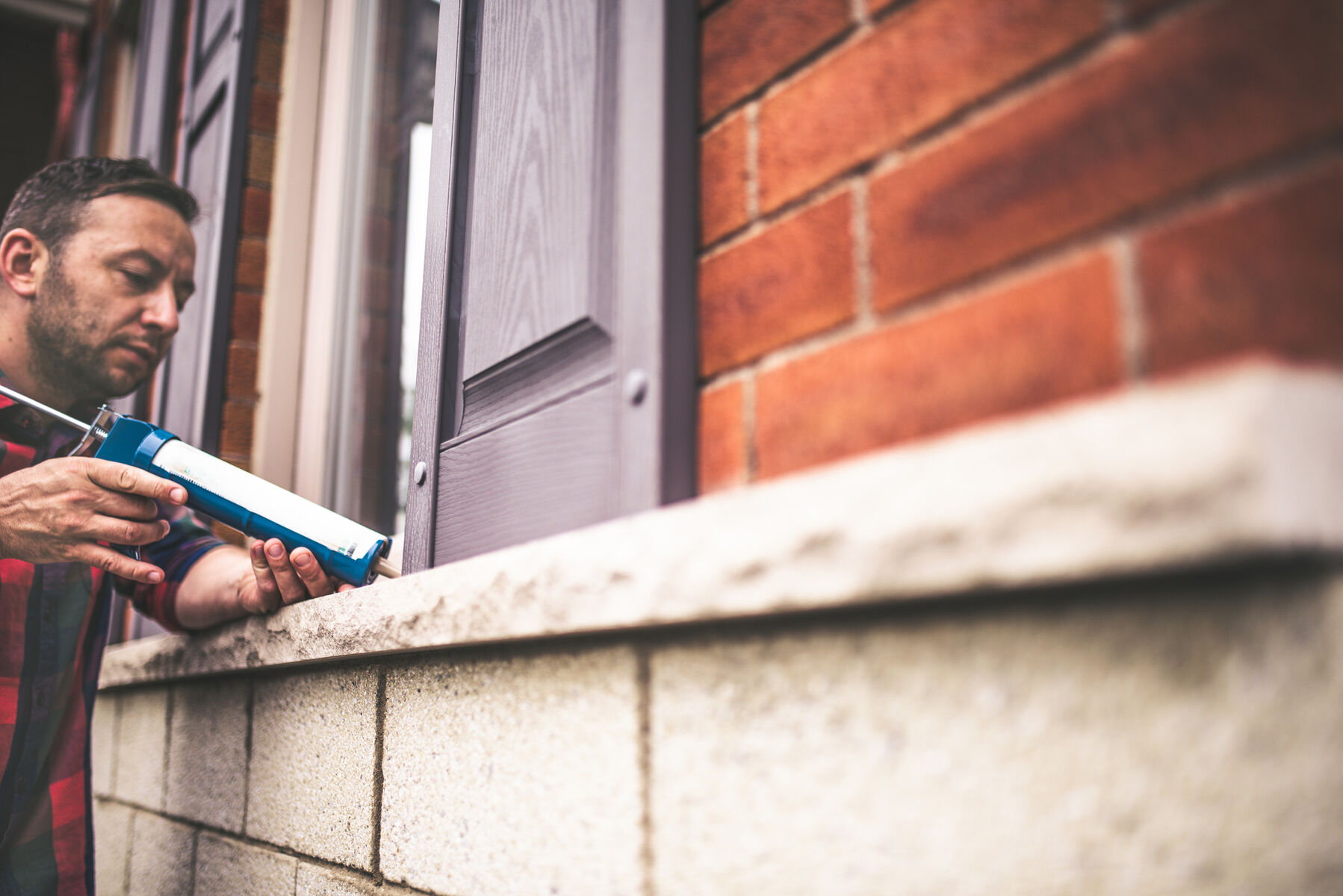 man caulking exterior leaks and cracks on his home with sealant