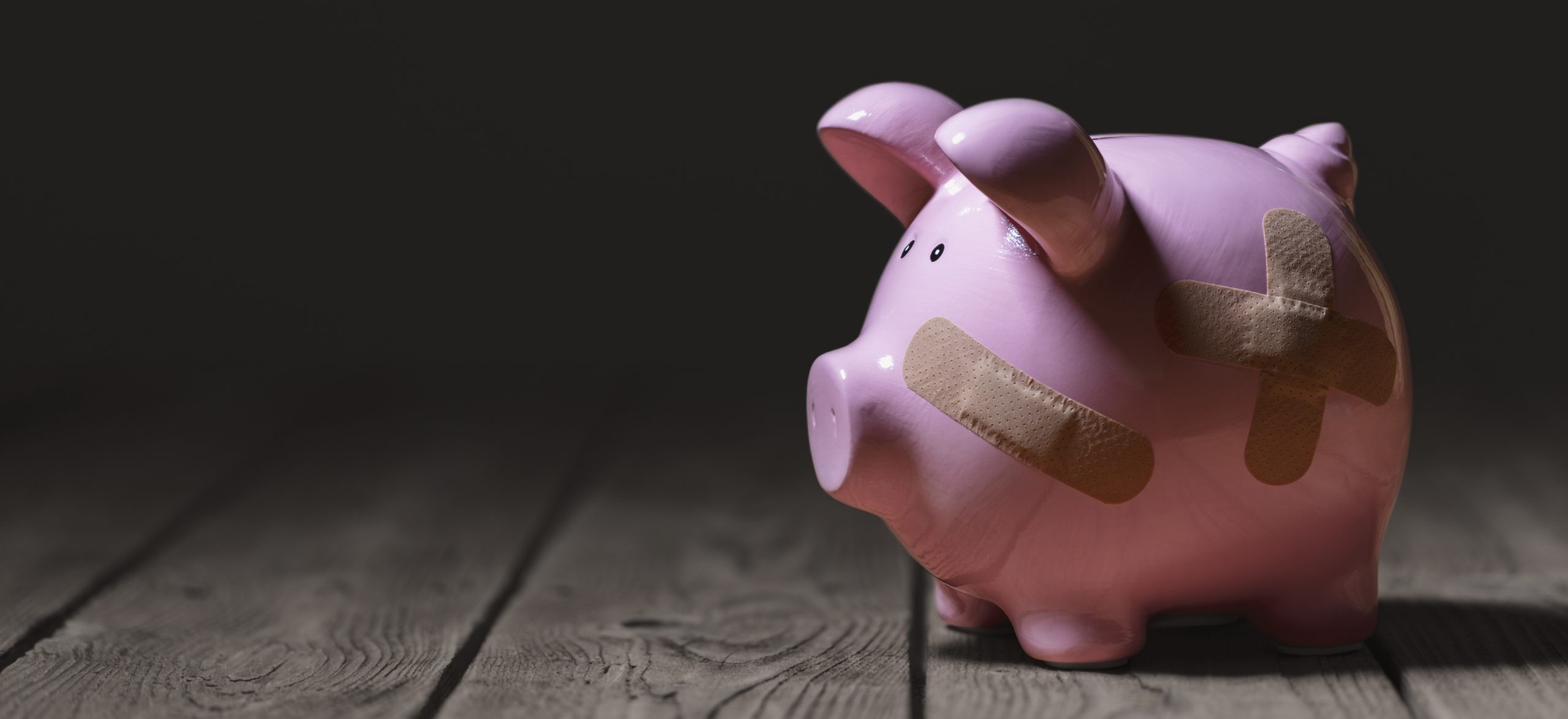A pink piggy bank with bandaids on dark background