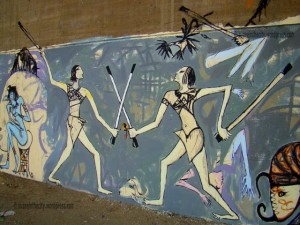 [On the AUC’s library wall, a mural of ancient figures and animals in battle by Alaa Awad represents the many violent protests and clashes that took place in the area.]