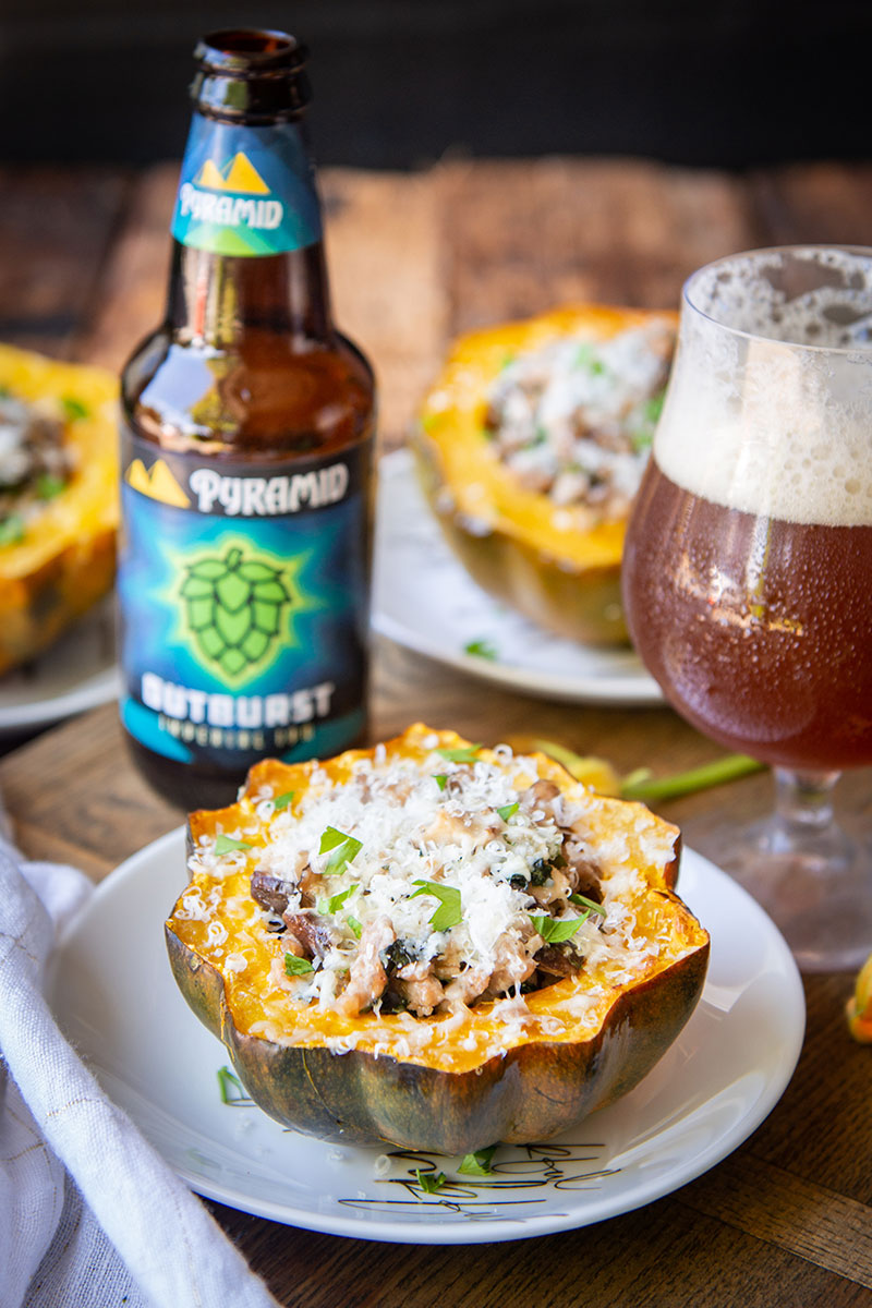 acorn squashes filled with sausage and kale on plates surrounded by a bottle of Outburst IPA