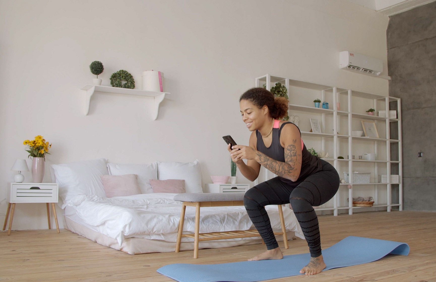 Woman doing leg squats in living room while looking at their phone