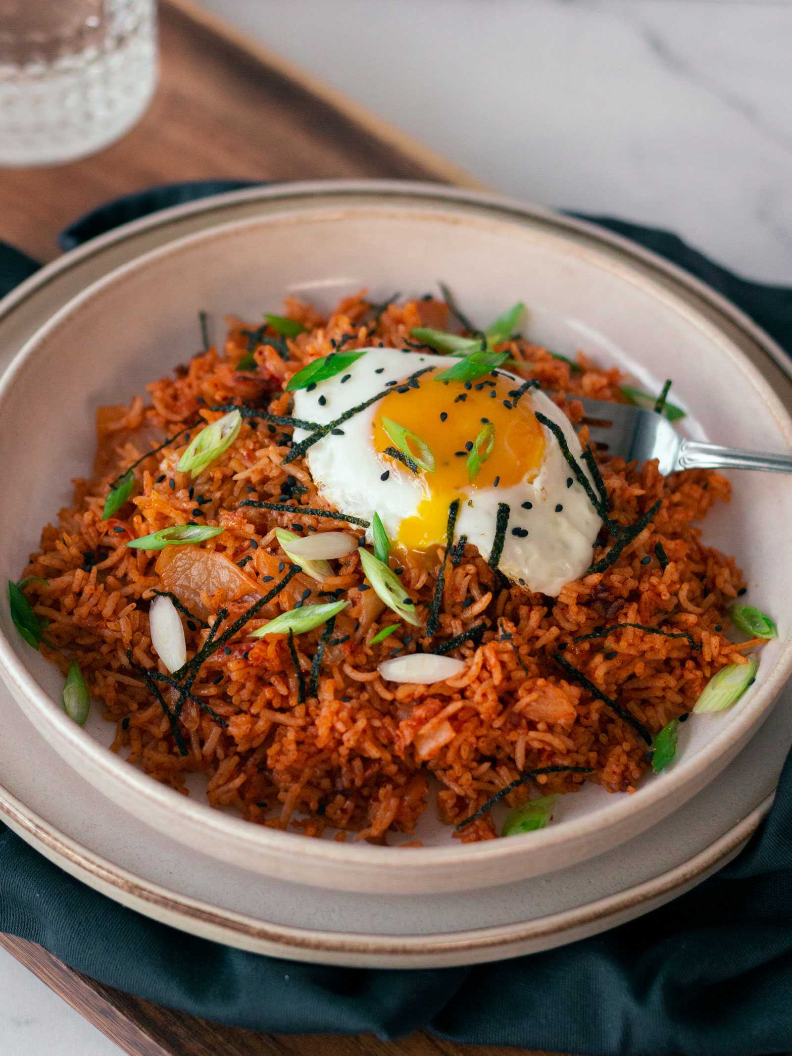 This image is of a bowl full of Kimchi Fried Rice, with a fried egg on top w/ fresh green onions sprinkled on top. This recipe is sweet and spicy with a serious tang. The gochujang makes each bite taste like the first with a hint of sweetness chasing away the lingering tang from the kimchi.