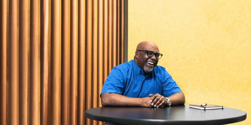 Man with black rim glasses wearing a blue shirt laughing while sitting at a table
