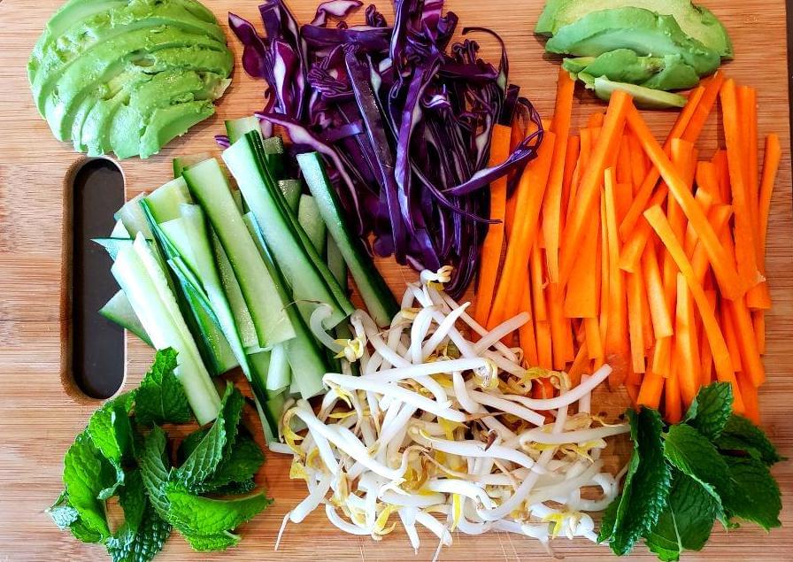 Cutting board with carrots, red cabbage, avocado, sprouts, mint, cucumber