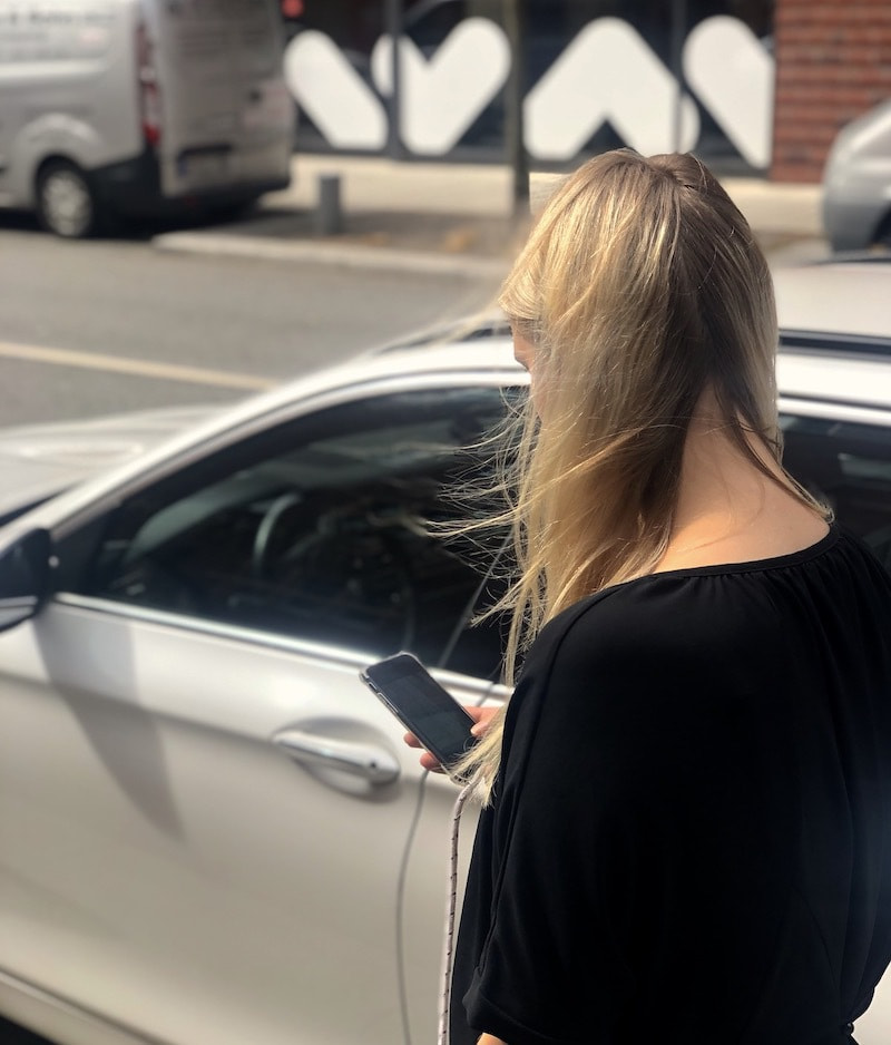 Blonde caucasian female standing in the middle of a road looking down on her mobile device.