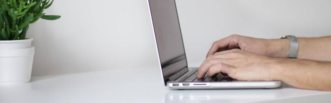 Schreibtisch mit Laptop und Pflanze Mann schreib am Laptop, der auf einem Schreibtisch mit einer Pflanze steht
