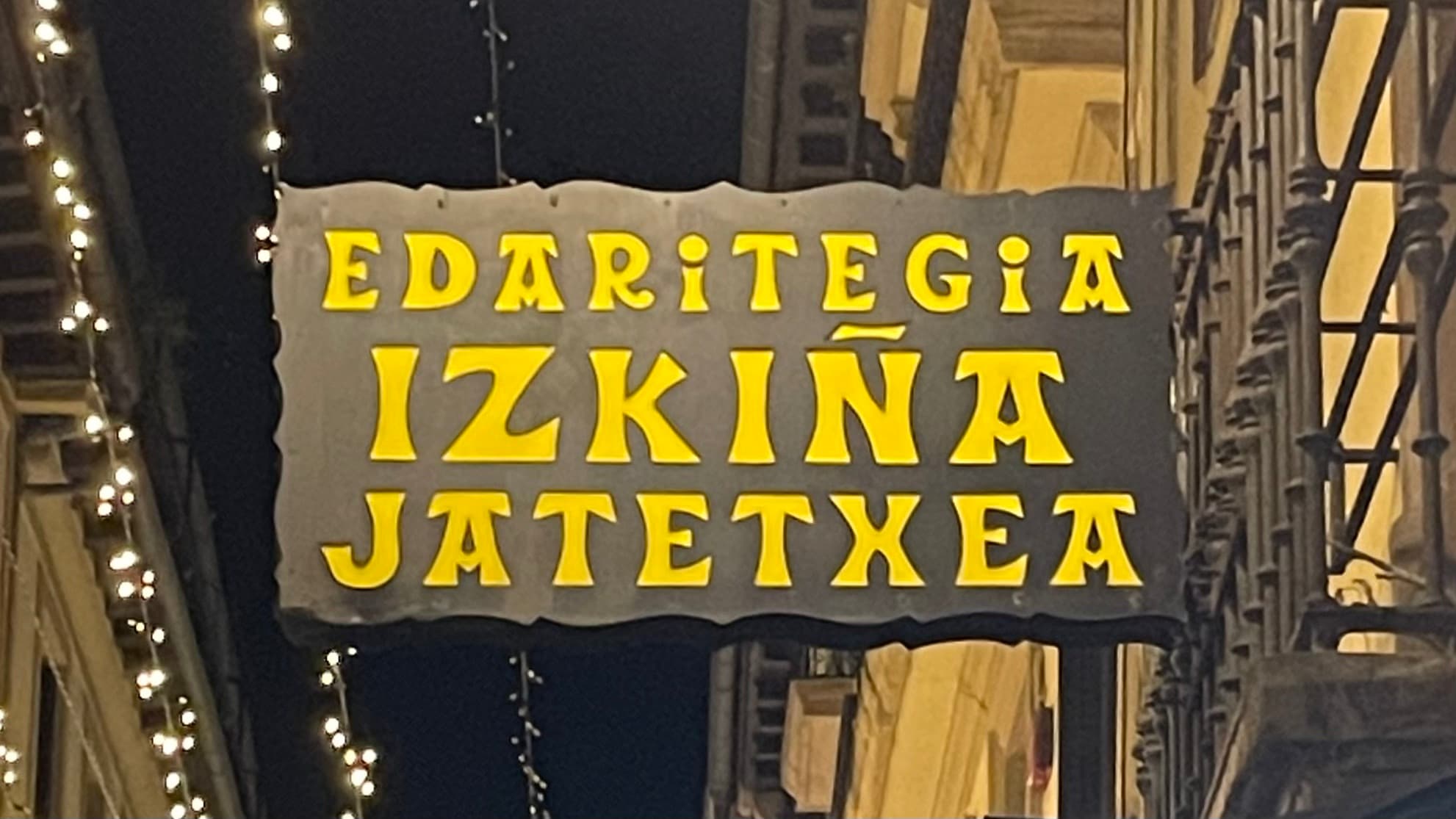 A storefront sign written in Basque with large, bold yellow letters on a black background