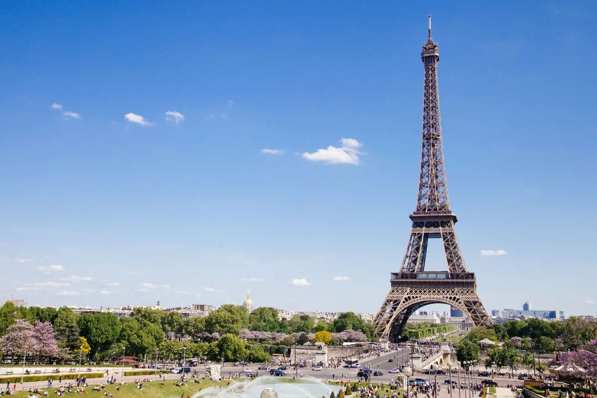 Foto mostrando a torre Eiffel por completo, de longe, em um dia ensolarado e de céu azul