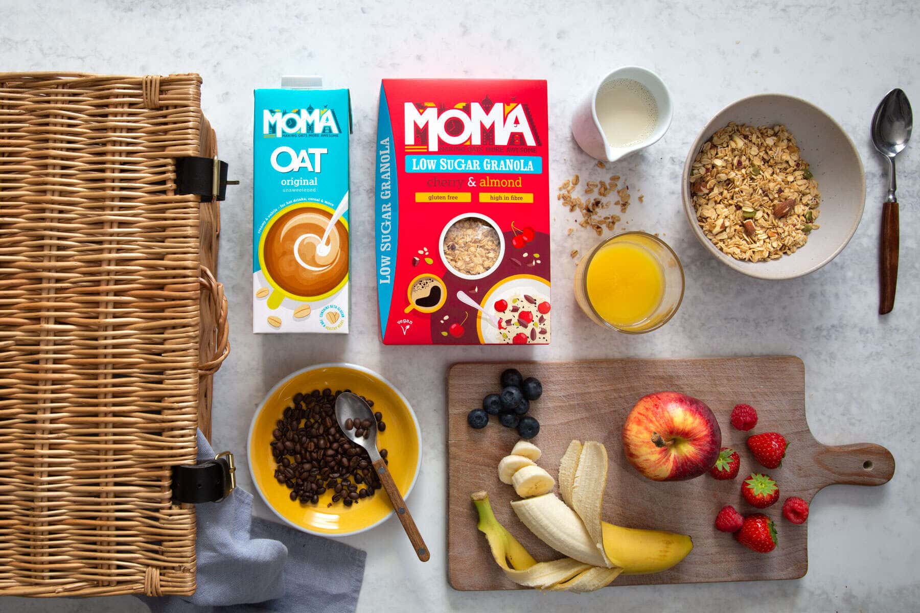 Moma food porridge and Oat milk with an assortment of breakfast condiments next to a picnic hamper
