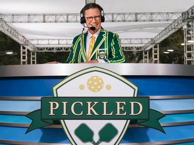 Host of Pickled, Stephen Colbert sitting at a podium in a Pickled coat with a headset on