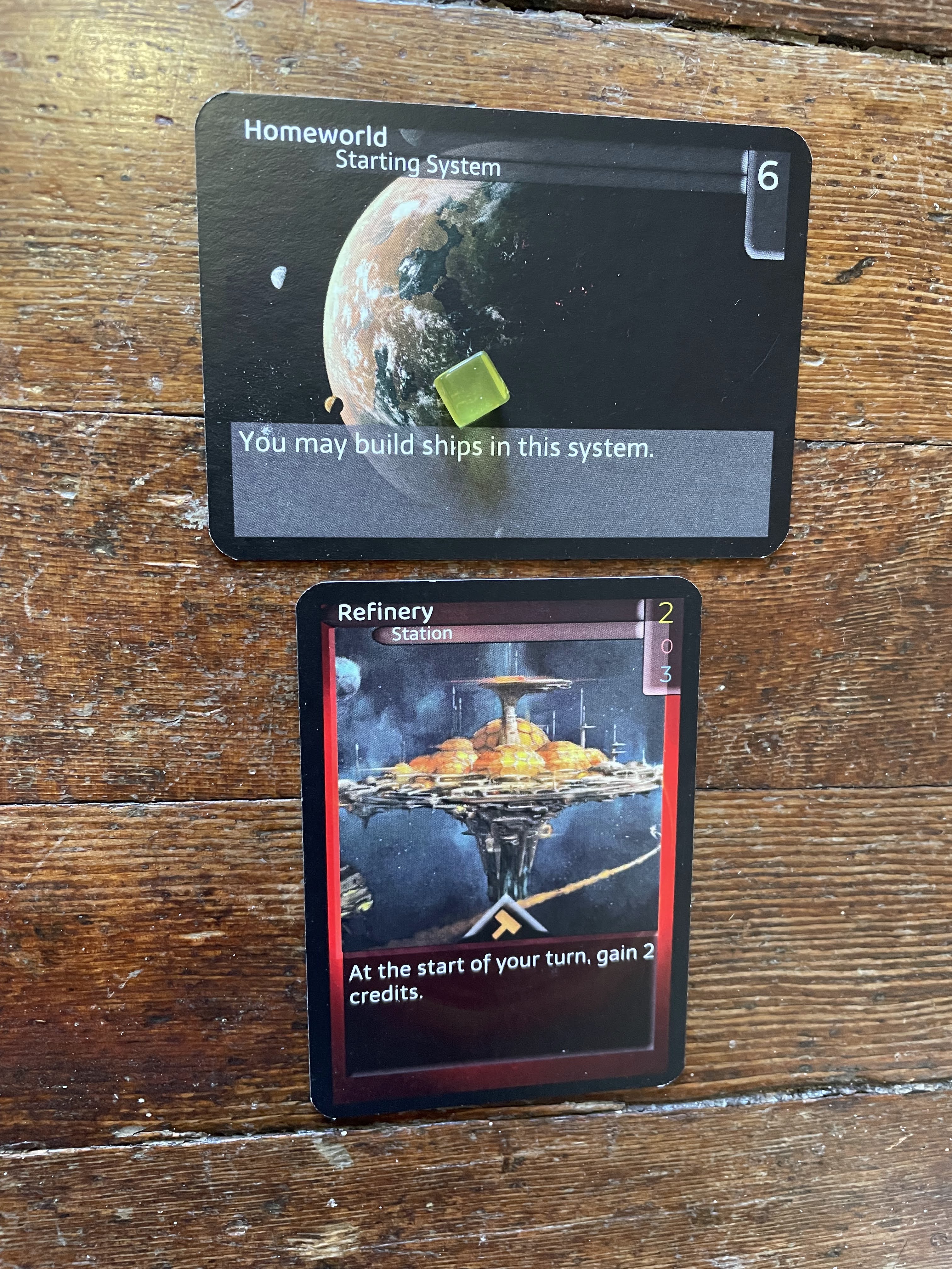 A Homeworld card, with a yellow counter on it, and a Refinery station card placed beneath it.