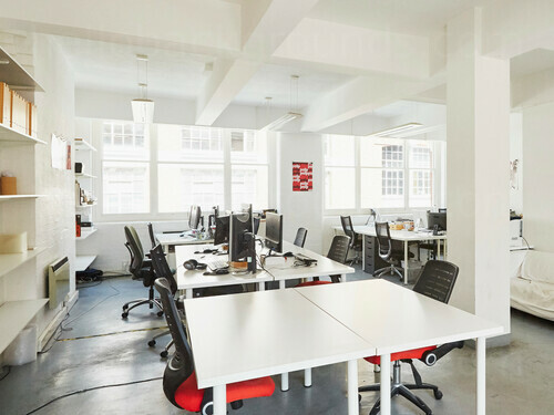 Contemporary pillared shared workspace containing white computer desks with black office chairs in front of large windows Zoom background