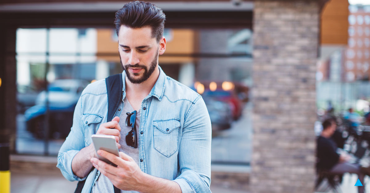 A man in a denim shirt using his phone while in front of a business. 