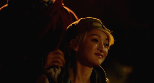 A screenshot of Angie (played by Zhou Xun) with blonde hair and a backwards baseball cap, riding a bike with an unknown figure standing on the bike behind her. From the film 'Women Who Flirt'.