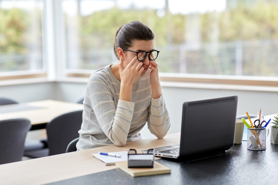 Woman rubbing her eyes, annoyed at her computer running so slow