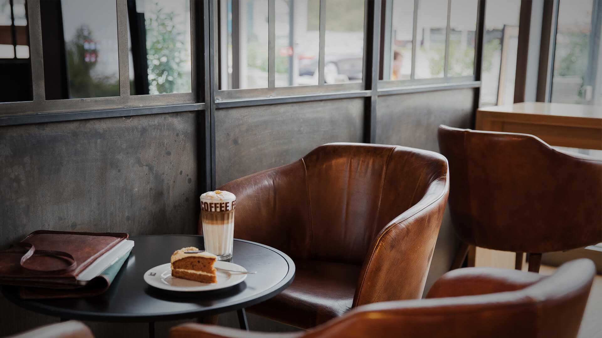 Sitzgelegenheit in einem Coffee Shop, ein Stück Kuchen und ein Latte Macchiato auf dem Tisch