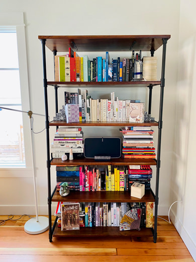 A bookshelf chock full of books arranged mostly in rainbow order. In the center of the bookshelf is a Sonos.