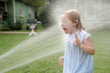 Little girl getting sprayed in the face by a hose.