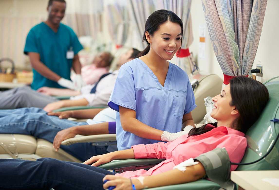 A phlebotomist assists someone giving blood.